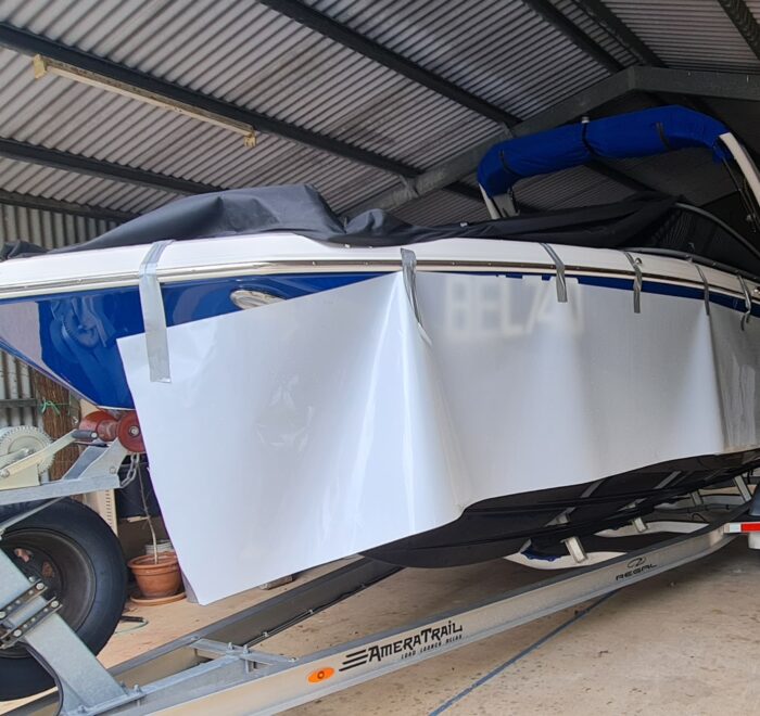 Marine vinyl wrap installation in progress on a Regal boat with white wrap film being applied to the hull